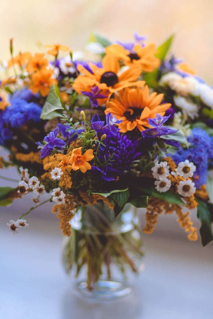 A colorful arrangement of wildflowers in a vase, featuring sunflowers and daisies with a blurred background.